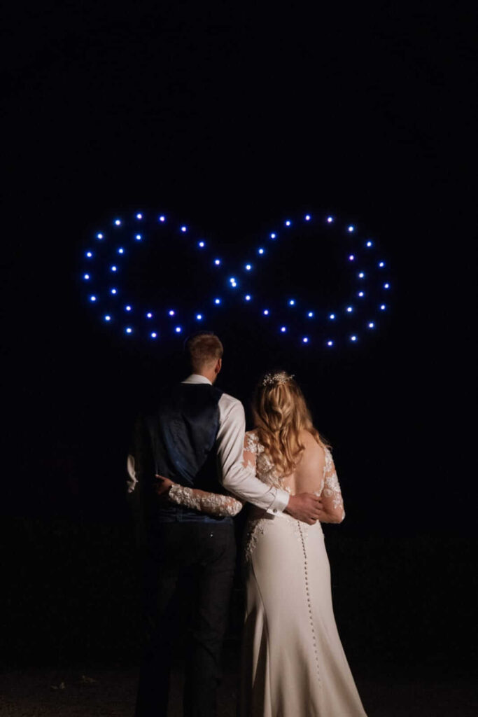 Newlyweds standing beneath an infinity symbol formed by drones